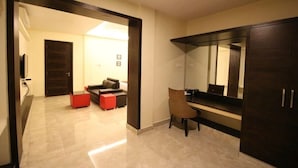 Una habitación de hotel moderna con un espejo grande, un escritorio y una zona de estar cómoda con sofá y reposapiés.