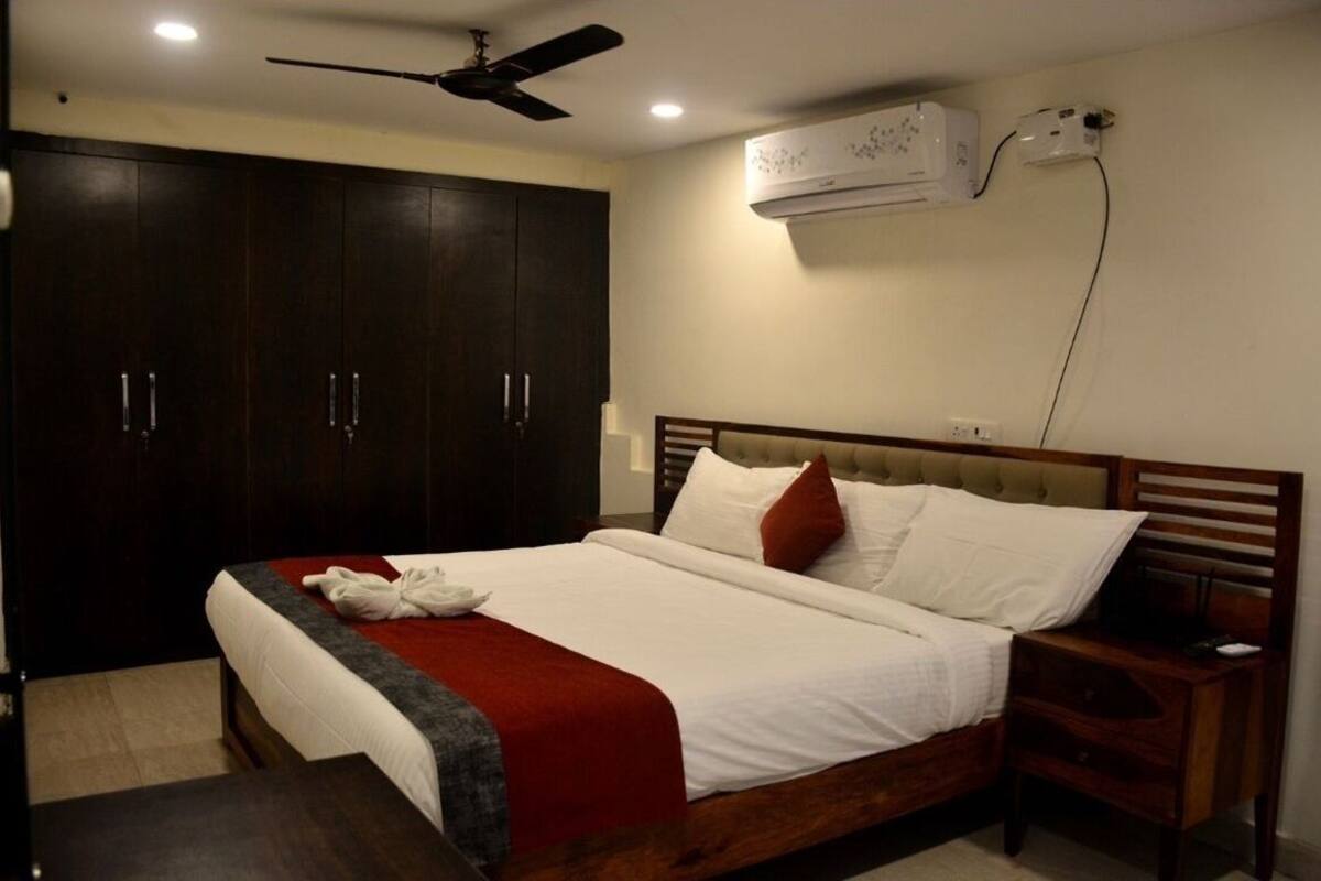 Een hotelkamer met een groot bed, een houten garderobe, plafondventilator, airconditioning en nachtkastje.