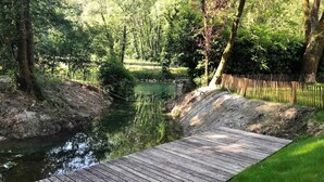 A wooden dock extending over a calm river, surrounded by lush greenery and a wooden fence.
