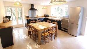 A spacious kitchen with a wooden dining table, modern appliances, and large windows allowing natural light.