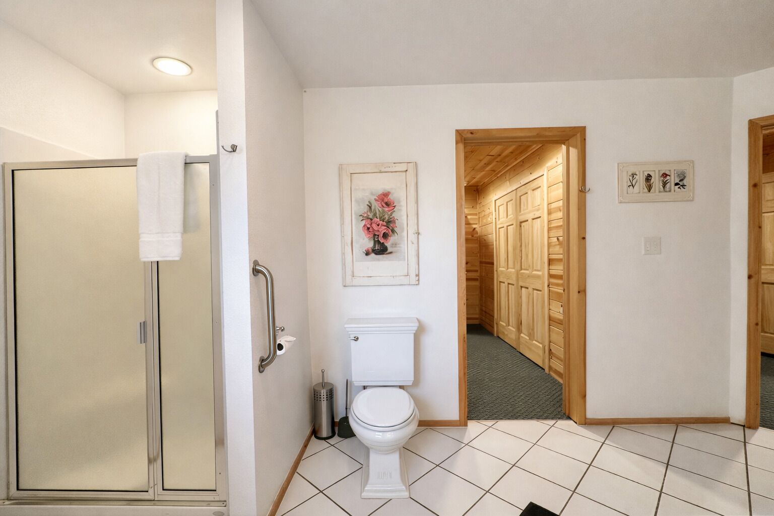 A bathroom with a shower, toilet, and a wooden hallway leading to a bedroom.