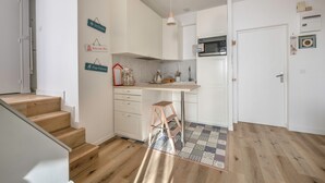 Una cucina compatta con mobili bianchi, uno sgabello di legno e un tappeto decorato.