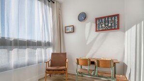 Una stanza con una sedia di legno, un tavolino, una sveglia e un quadro appeso al muro.