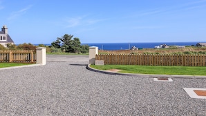 A gravel driveway leading to a property with a wooden fence and a view of the sea. - No. 29 Ness (Isle of Lewis)