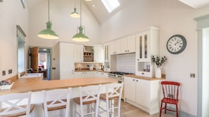 A spacious kitchen with a large island, white cabinetry, and a red chair. - No. 29 Ness (Isle of Lewis)