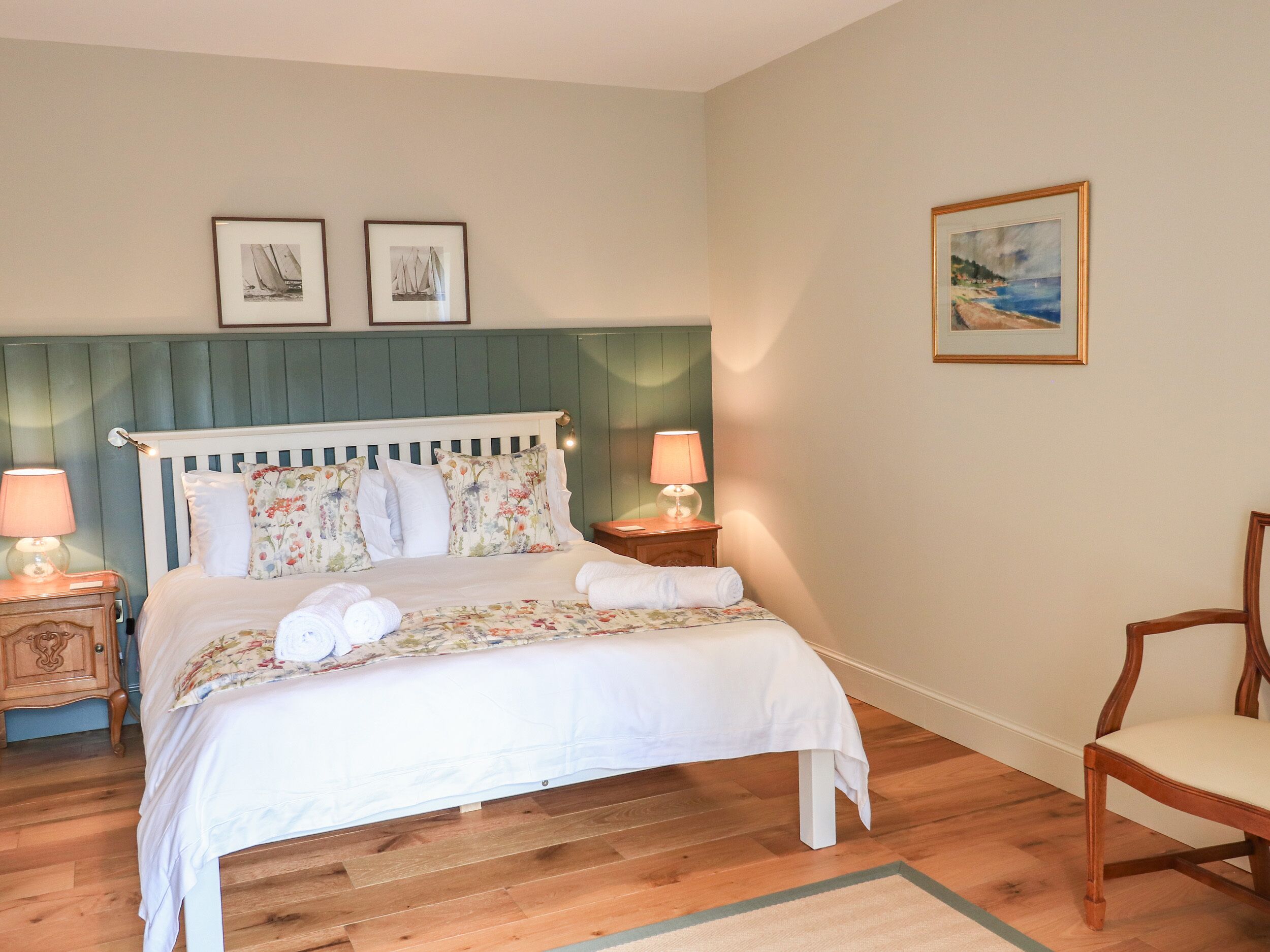 Una cama bien hecha con ropa de cama floral, una mesita de noche de madera con una lámpara y un cuadro en la pared.