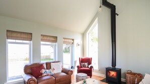 A living room with a brown leather sofa, a red armchair, a wooden coffee table, and a black wood-burning stove. - No. 29 Ness (Isle of Lewis)