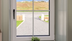 A view through a window with a view of a road, a grassy area, and houses in the distance. - No. 29 Ness (Isle of Lewis)