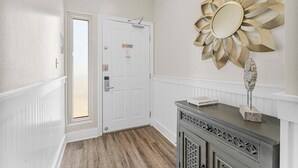 Un pasillo con una puerta blanca, un espejo decorativo con forma de sol y un mueble con una escultura de piedra.