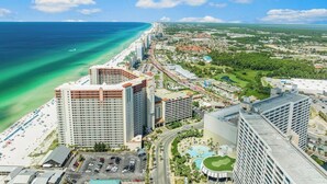 Un paisaje urbano costero con un hotel frente a la playa, una autopista y vegetación circundante.