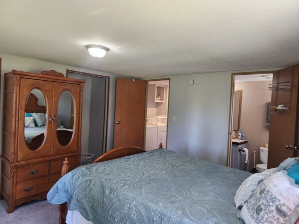 A bedroom with a large wooden wardrobe, a bed with a patterned bedspread, a bathroom with a toilet and sink, and a ceiling light. - Georgie's Getaway! Beautiful stay on 6 acres just minutes from the lakeside (Fort gibson)