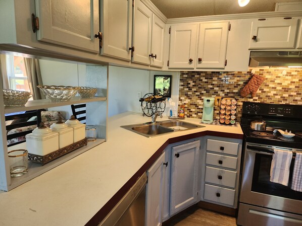A kitchen with white cabinets, a stainless steel sink, a coffee maker, and a stove.