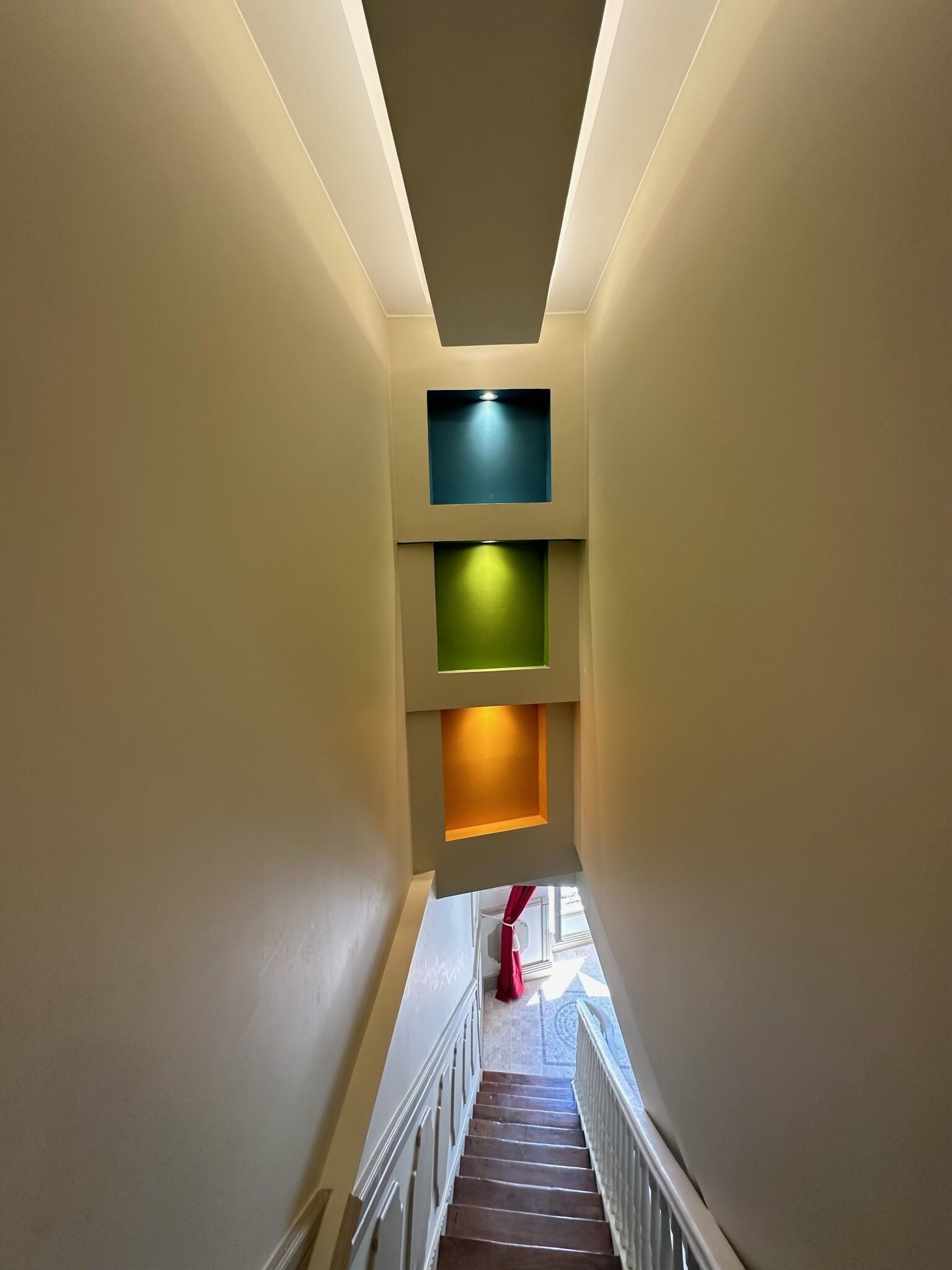 Una escalera estrecha con barandilla que conduce a un rellano con ventana.