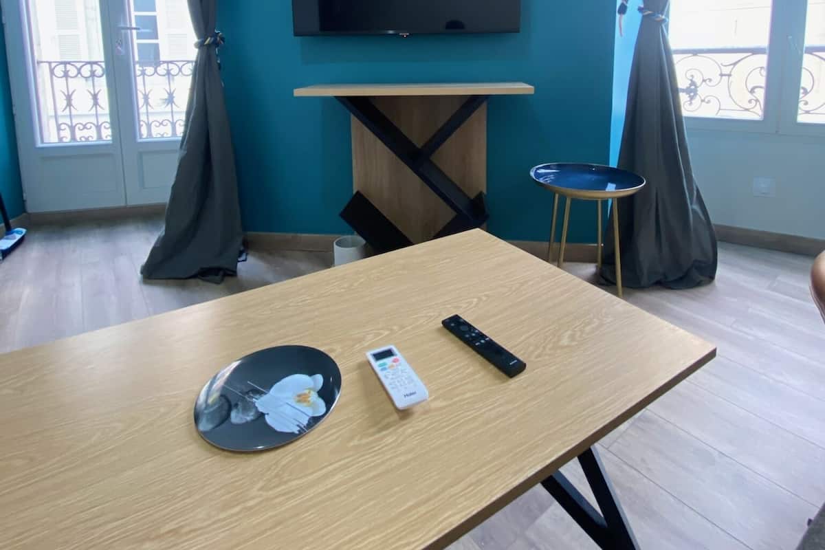Una habitación con una mesa de madera, un televisor montado en la pared y una ventana con cortinas.