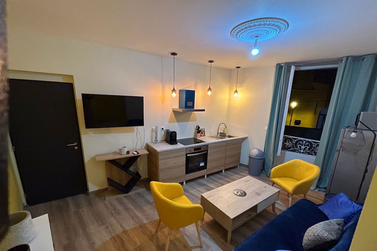 Un espacio habitable compacto con kitchenette, un sofá, una mesa de centro y un televisor montado en la pared.