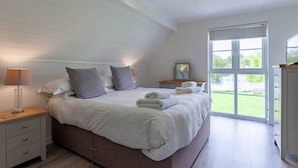 Une chambre à coucher avec un grand lit, des tables de chevet, une commode et une fenêtre donnant sur un paysage verdoyant.
