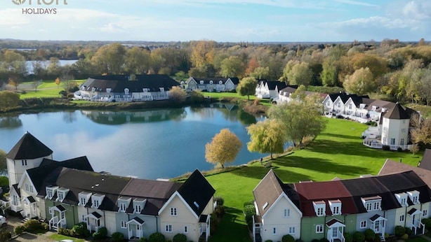 Un quartier résidentiel où les maisons sont disposées autour d’un lac, et où l’on trouve un mélange de bâtiments à un ou plusieurs étages, avec différents types de toits.