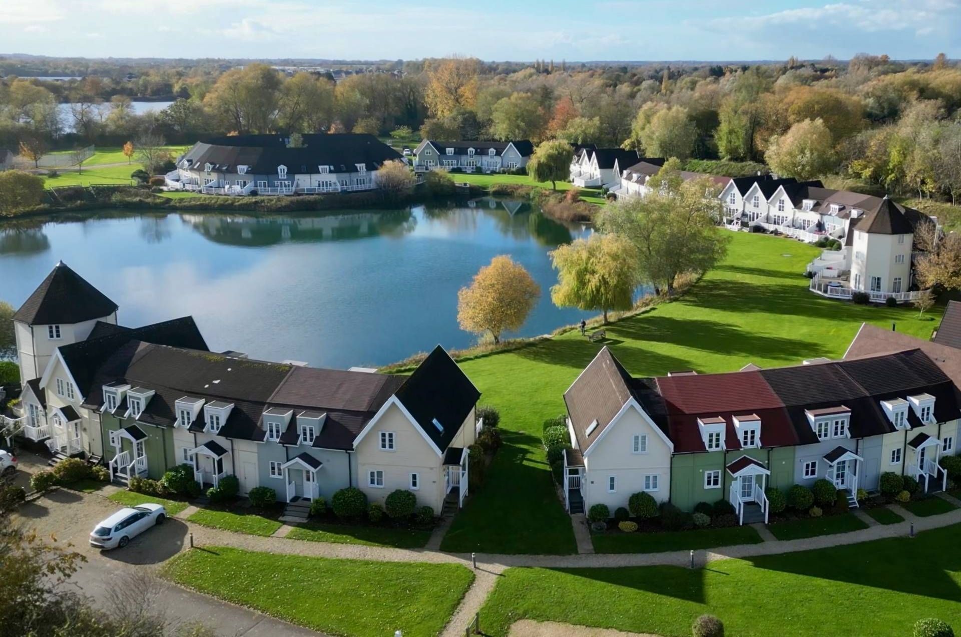 Zona residencial con casas dispuestas alrededor de un lago, que presenta una combinación de construcciones de uno y varios pisos con diferentes estilos de techo.