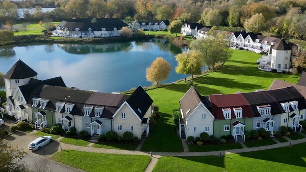 A residential area with houses arranged around a lake, featuring a mix of single and multi-story buildings with various roof styles. - Isis Lakes 55, Lakeside Lodge - Lakeside Lodge, On-Site Activities, Sleeps 6 (South Cerney)