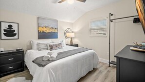 A bedroom with a bed, bedside table, lamp, artwork, and a ceiling fan. - SoHo Suite by Brightwild | Steps to SoHo! (Tampa)