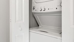 A white washer and dryer unit with a door open, revealing a storage area with purple containers. - SoHo Suite by Brightwild | Steps to SoHo! (Tampa)
