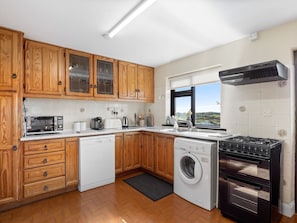 Una cocina con armarios de madera, lavavajillas, lavadora, estufa y ventana con vistas.