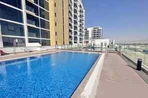 Un área de piscina en la azotea con una piscina azul cristalina, rodeada de edificios modernos con balcones.