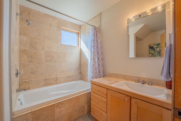 A modern bathroom with a bathtub, a shower, a vanity with a sink, and a mirror with lights.