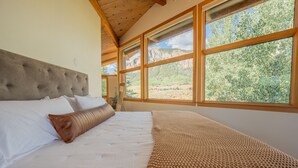 Un dormitorio con una cama grande, un cabecero de madera y varias ventanas con vistas a un paisaje montañoso.