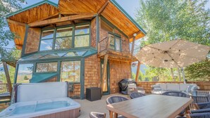 Una cabaña de madera con jacuzzi, asientos exteriores y una sombrilla grande.