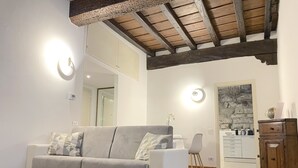 A modern living room with a grey sofa, wooden beams on the ceiling, and a stone wall. - Tower Gombito's Apartment (Bergamo)