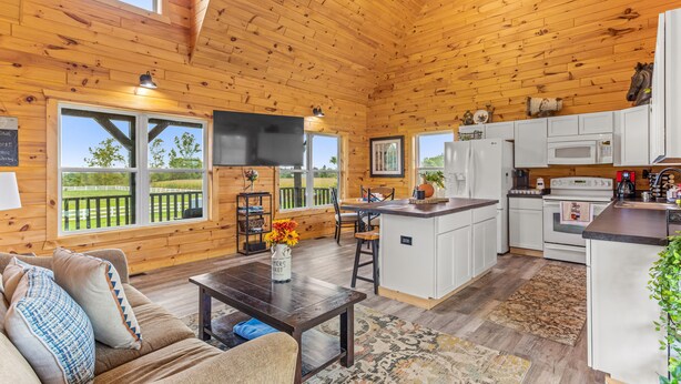 Une cabane spacieuse avec un intérieur en bois, un coin repas, une cuisine et de grandes fenêtres donnant sur une courClose.
