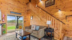 Une pièce chaleureuse avec un escalier en bois, un canapé, une table basse et une vue sur l’extérieur.