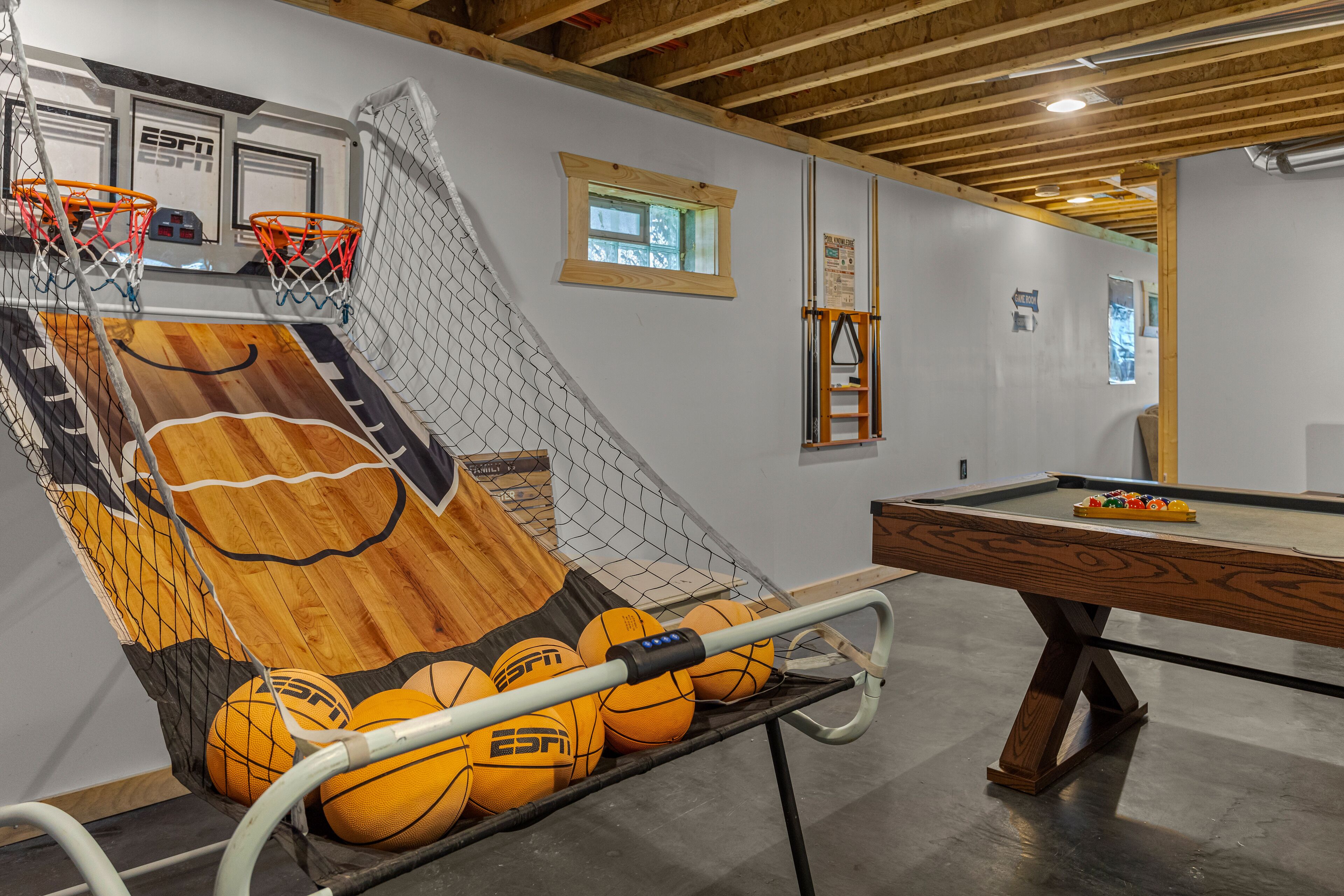 A basketball court with a wooden floor, a net, and a pool table in a room with wooden beams and a window.