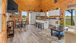 Une cabane en bois comprenant une cuisine, un coin repas et offrant une vue sur l’extérieur.