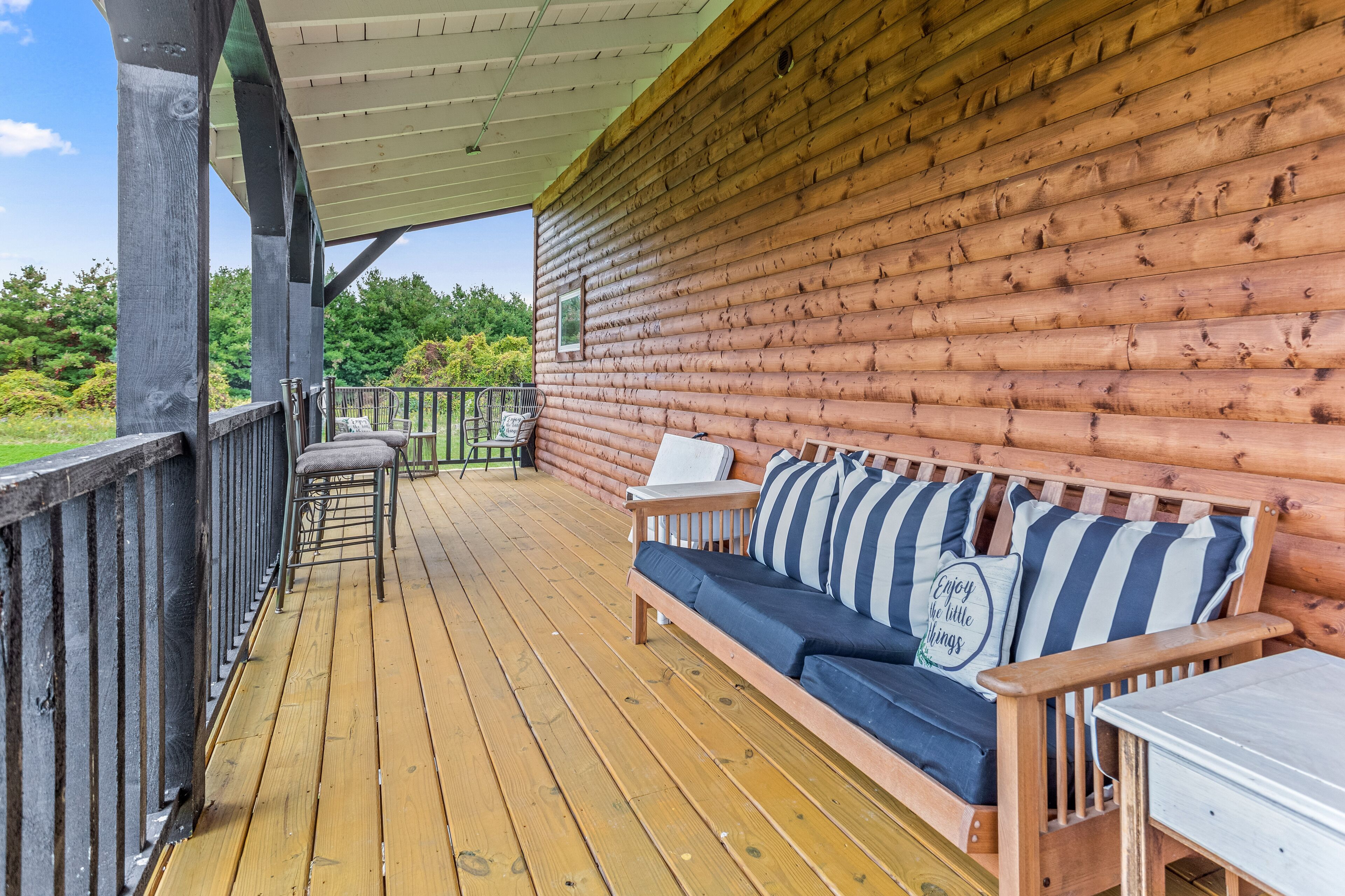 Une terrasse en bois avec un canapé et des fauteuils, une petite table et une rambarde.