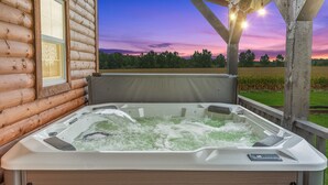 Un bain à remous avec, en arrière-plan, un chalet en bois et une vue sur les champs.