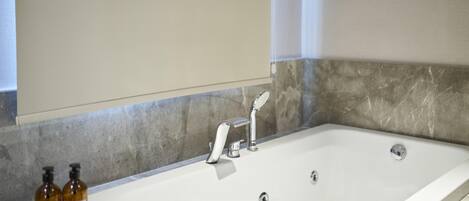 A modern bathroom with a large bathtub, a mirror, and two bottles of shampoo on the counter.