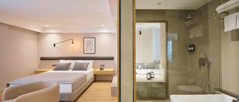 Una habitación de hotel moderna con cama, mesita de noche, silla y zona de ducha con paredes de vidrio.