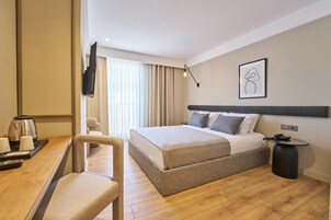 Habitación de hotel con cama, mesita de noche, silla y escritorio con cafetera y tazas.