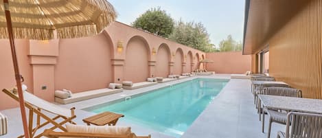 A poolside area with lounge chairs, a thatched umbrella, and a pool.