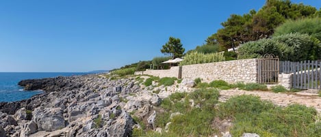 A coastal property with a stone wall, a wooden fence, and a view of the sea.