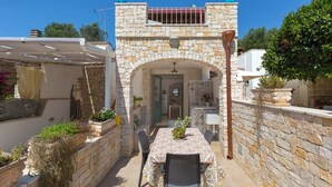 A stone-walled outdoor dining area with a table and chairs, a covered seating area, and potted plants.