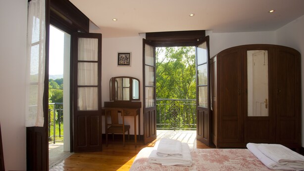 A bedroom with a large bed, a desk, and a view of a balcony with a railing. - Villa Victoria (AS)