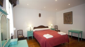 A neatly arranged bedroom with a large bed, two bedside tables with lamps, a small table, and a mirror. - Villa Victoria (AS)