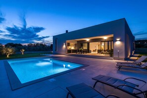 Una casa moderna con piscina, mobiliario exterior y una entrada bien iluminada.