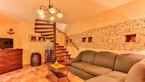 A cozy living room with a stone wall, a wooden staircase, a sofa, a TV, and a decorative table. - Villa Edera in Sveti Kirin (Sveti Kirin)