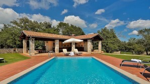 A rectangular swimming pool with clear blue water, surrounded by a wooden deck. There are lounge chairs and a covered patio area with stone pillars and a tiled roof. - Villa Edera in Sveti Kirin (Sveti Kirin)
