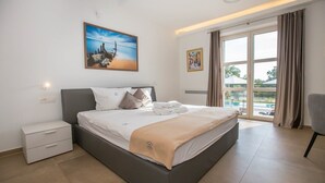 Una habitación de hotel moderna con una cama grande, una mesita de noche, una silla y un balcón con vistas.