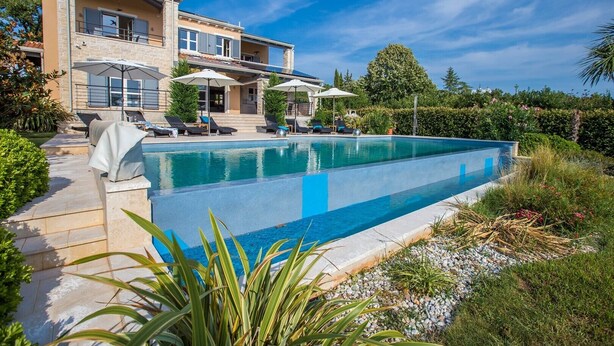 Una casa moderna de dos pisos con piscina, mobiliario de exterior y un jardín bien cuidado.